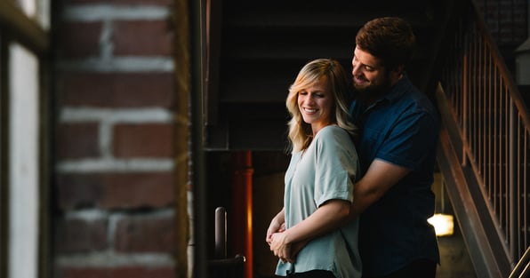 Husband holding wife by stairs in home