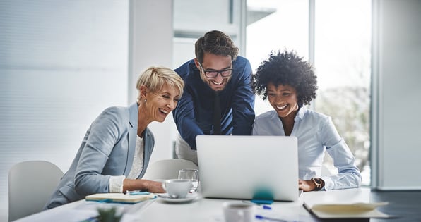 three employees surrounding a desk looking at a computer