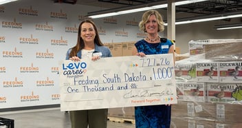 Two women hold a check from Levo Cares Foundation for Feeding South Dakota at their distribution center
