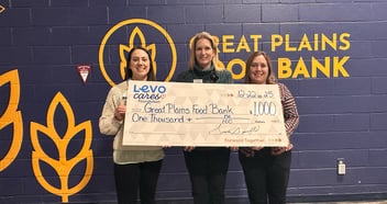 Three women hold a check from Levo Cares Foundation with a donation for $1000 in front of Great Plains Food Bank in Fargo.