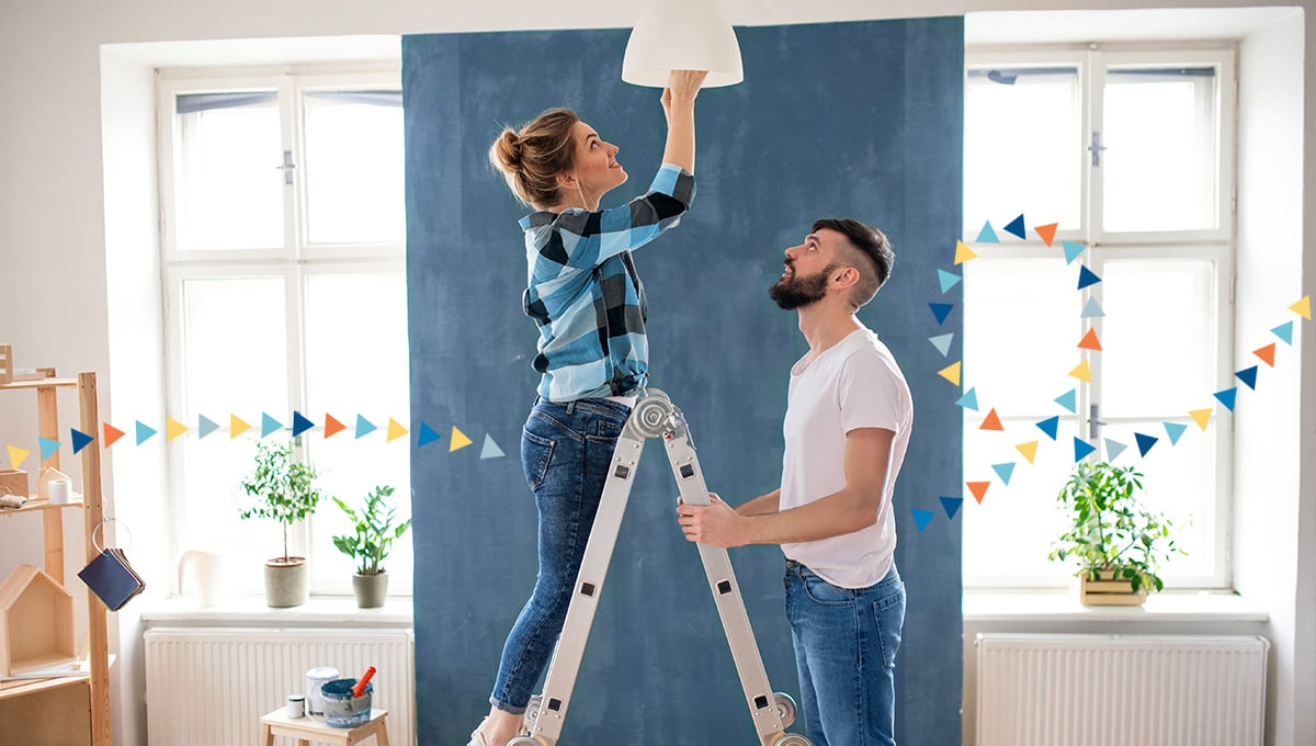 a woman installing a lightbulb while a man holds a ladder in front of a room being renovated. a woman installing a lightbulb while a man holds a ladder in front of a room being renovated.