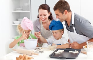 Happy family cooking a cream together in the kitchen while little boy adding sugar in the preparation