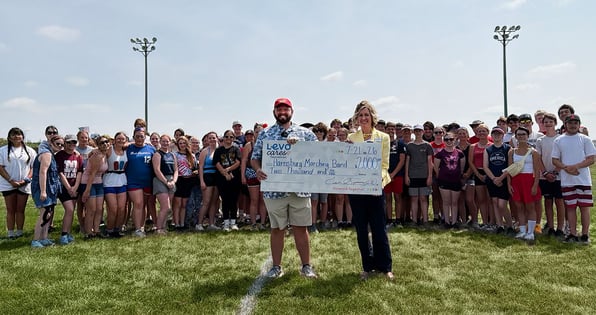 Two people hold a check from Levo Cares Foundation in front of the Harrisburg High School Marching Band