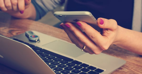 Woman holding phone over laptop