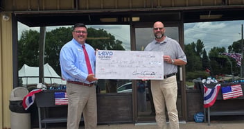 Two people holding a Levo Cares Foundation check in front of Mid-Step Services in Sioux City, IA