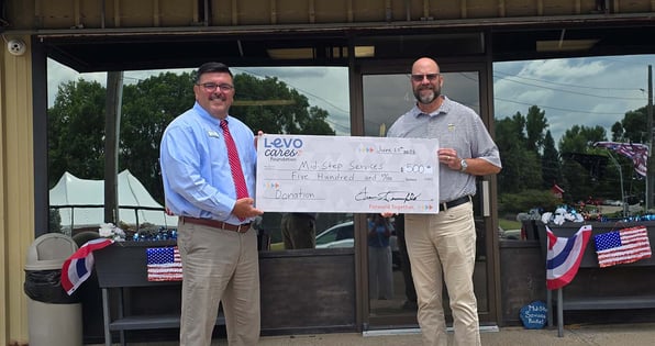Two people holding a Levo Cares Foundation check in front of Mid-Step Services in Sioux City, IA