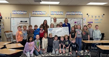 Teacher surrounded by her students accepting a $500 Adopt A Classroom award