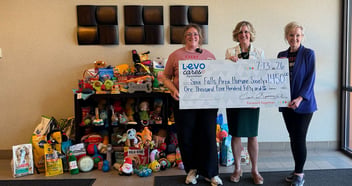 three women hold a check from Levo Cares Foundation for the Sioux Falls Area Humane Society in front of a large number of toys and pet supplies