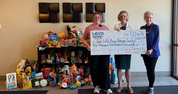three women hold a check from Levo Cares Foundation for the Sioux Falls Area Humane Society in front of a large number of toys and pet supplies