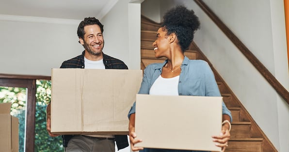 A couple in a home carrying two cardboard boxes