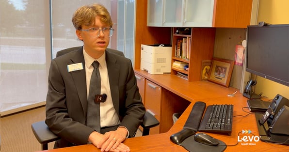 A man sitting behind a desk with a computer looking at the camera